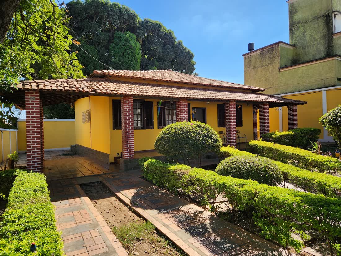 A casa amarela da Perfil Estética vista do jardim, com varanda de colunas de tijolinho e jardim podado